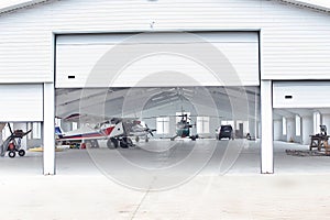 Small single prop engine aircrafts planes parked inside workshop hangar with opened door.