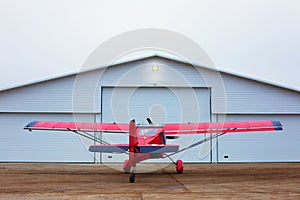 Small single prop engine plane parked in front of workshop hangar