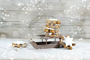 Small sleigh with a stack of cinnamon stars on a rustic grey wooden background with snowy bokeh light spots and copy space,