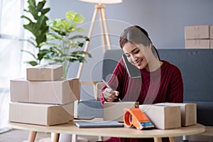 A small SME business owner receives product orders and writes shipping information on cardboard boxes in the home office