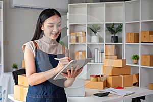 A small SME business owner receives product orders and writes shipping information on cardboard boxes in the home office