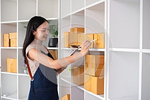 A small SME business owner receives product orders and writes shipping information on cardboard boxes in the home office