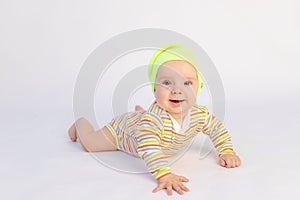 Small smiling baby girl 6 months old lies on a white isolated background in a bright bodysuit and yellow hat, space for text