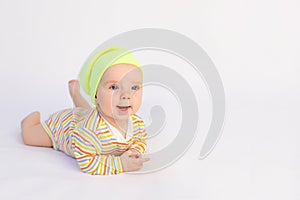 Small smiling baby girl 6 months old lies on a white isolated background in a bright bodysuit and yellow hat, space for text