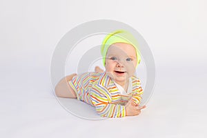 Small smiling baby girl 6 months old lies on a white isolated background in a bright bodysuit and yellow hat, space for text