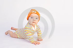 Small smiling baby girl 6 months old lies on a white isolated background in a bright bodysuit and yellow hat, space for text