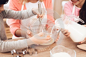 Small smiling boy is whipping eggs in bowl with his sister and grandmother