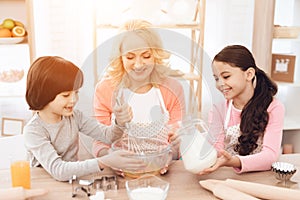 Small smiling boy is whipping eggs in bowl with his sister and young grandmother