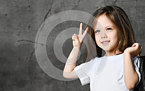 Small smiling cute girl in black and white rock style clothing standing and showing peace and victory sign with fingers