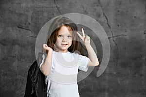 Small smiling cute girl in black and white rock style clothing standing and showing peace and victory sign with fingers