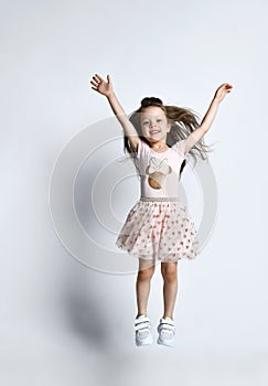 Small smiling cute girl in casual summer dress and sneakers jumping over white wall background