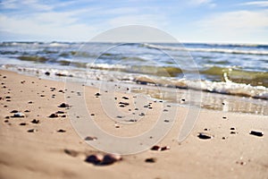 Small smooth pebbles lie on the sand near the shoreline. Selective focus