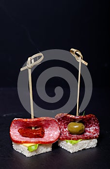 Small snacks canape with salami, bread and lettuce on skewer on