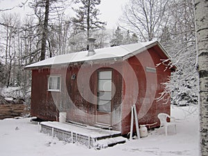 A small snow-covered cabin in a birch forest with a recent light snowfall powdering the surfaces photo