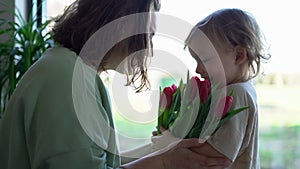 Small son is giving beautiful flower to his mother, little child boy flower preparing nice surprise for his mum look