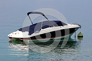 Small speed boat covered with dark blue protection anchored in local harbor surrounded with calm clear blue sea