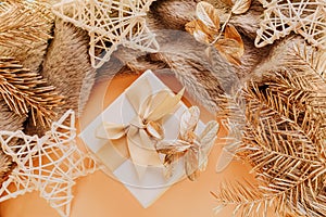 A small square gift with a bow close-up. Nearby is a plaid, golden Christmas tree branches,