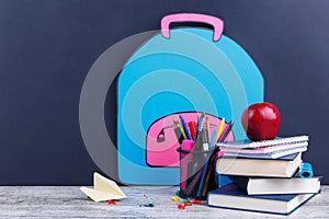 A stack of books, stationery and a apple, on a background with an image of a paper backpack. The concept of education.