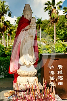 A small statue of the goddess Guanyin with a baby in her arms in Nanshan Park. The small box says: `for donations.` Hainan.