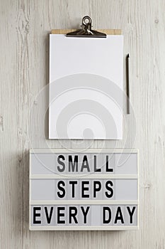 `Small steps every day` words on a lightbox on a white wooden background, top view. Overhead, from above, flat lay