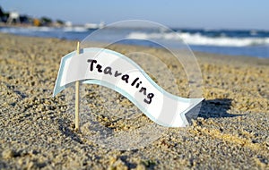 Small stick with paper speech bubble with word Traveling stands on sandy beach