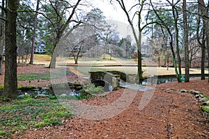 A small stone bridge covered in algae over a lake with lush green and autumn colored trees reflecting off the lake water