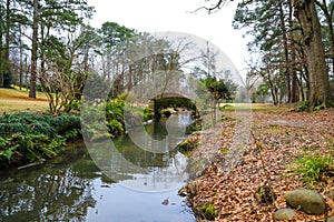 A small stone bridge covered in algae over a lake with lush green and autumn colored trees reflecting off the lake water