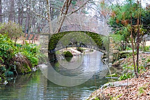 A small stone bridge covered in algae over a lake with lush green and autumn colored trees reflecting off the lake water