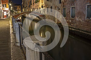 Small stone bridge spanning the Venetian canal by night