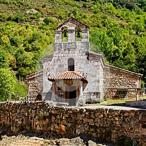 Small stone chapel next to ancient stone wall in the green field. Asturias Spain