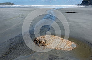 Small stream flowing past exposed stone on deserted unspoiled beach