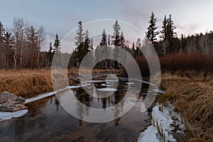 Small stream with ice on banks at sunset