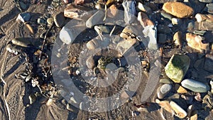 Small stream of water flowing through pebbles on a sand beach, towards the sea