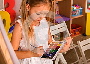 Small student girl painting in art school class.