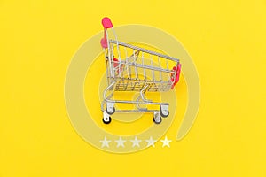 Small supermarket grocery push cart for shopping toy with wheels and 5 stars rating isolated on yellow background. Retail consumer