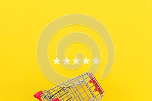 Small supermarket grocery push cart for shopping toy with wheels and 5 stars rating isolated on yellow background. Retail consumer