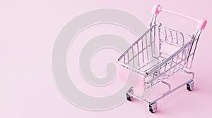 Small supermarket grocery push cart for shopping toy with wheels and pink plastic elements on pink pastel color paper flat lay