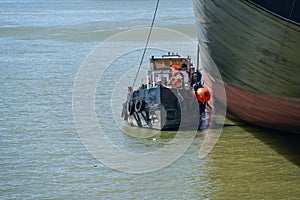 Small tanker boat or bunker barge at the hull of a large container ship taking over oil residues and wastewater in the industrial