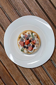 Small tart with buscuit, berries and mint on white plate on wood lath table photo