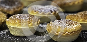 Small tartlets pastries with almond frangipane and powdered sugar over black stone surface