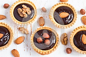 small Tarts with chocolate and different nuts on a white background, top view, closeup