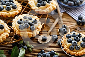 Small tarts made of puff pastry with addition fresh blueberries and caramel chocolate custard on a wooden rustic table, close up.
