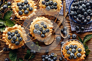 Small tarts made of puff pastry with addition fresh blueberries and caramel chocolate custard on a wooden rustic table, top view,