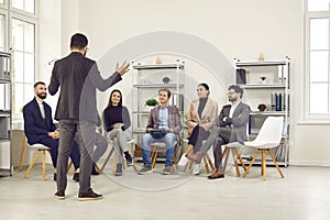 Small team of business people are listening to male speaker speaking in front of them in office.