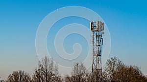 Small telecommunications tower set against a blue sky with a treeline