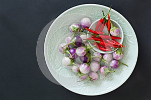 Small thai eggplants and red hot chili peppers on a green plates on a black background. Top view, asian food concept