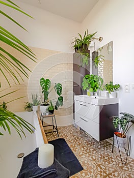 Small tiled bathroom with a bath and multiple green potted plants creating a tropical oasis