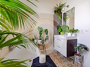 Small tiled bathroom with a bath and multiple green potted plants creating an urban jungle feeling