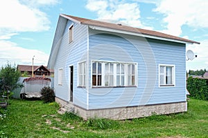 Small tiny wooden frame house painted in blue and white windows and door as a country residence in sunny summer day