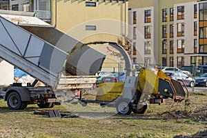 A small tipper with high sides together with a yellow wood chipper. The wood chipper shreds the branches and the wood chips are